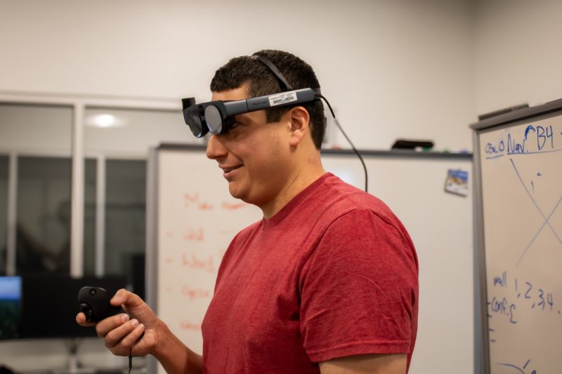 Brendan David-John wearing an eye-tracking device while holding the device's remote control.